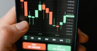 Hand holding smartphone displaying cryptocurrency trading graph in app.
