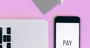 Top view of mobile payment setup with smartphone, credit cards, and laptop on pink background.