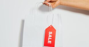 A person's hand holding a white shopping bag with a red sale tag on a white background.