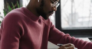 Young man wearing glasses and earbuds concentrating on a project indoors.
