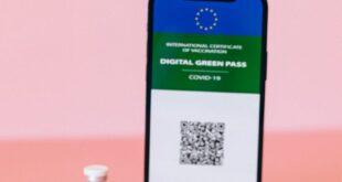 Smartphone displaying digital COVID-19 green pass with vaccine vial on pink background.