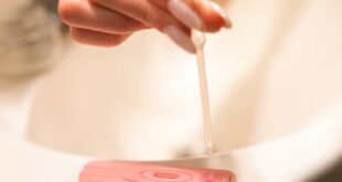 A hand using a pipette on a pregnancy test kit in a bathroom setting.