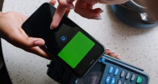 A close-up of a smartphone making a contactless payment on a terminal in a cafe setting.