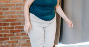 Full body of plus size female in activewear standing on weighing scales near brick wall in spacious gym after training