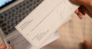 Individual holding a cheque over laptop, signifying online banking or financial transaction.