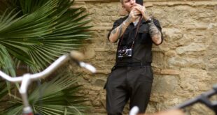 From below of young man in trendy clothes standing near stone wall and browsing smartphone while resting on street during trip
