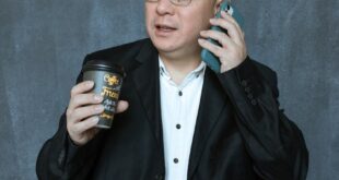Confident businessman holding coffee while on a phone call against a textured wall backdrop.