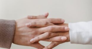 Crop unrecognizable female friends in casual outfit holding hands in light apartment near white wall