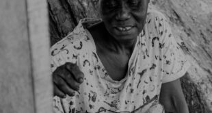 A candid black and white photo of an African woman grilling plantains outdoors in Ghana.