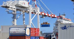 Colorful shipping containers stacked in a busy port with cranes overhead.