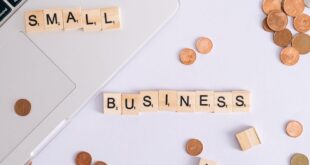 Flat lay of coins, Scrabble tiles spelling 'small business', and laptop, perfect for finance or entrepreneurship themes.