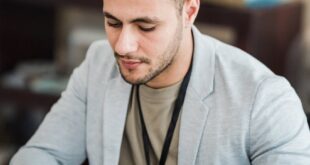 A young professional in a suit works intently on a laptop and tablet at an office desk.