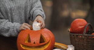 Woman preparing a carved pumpkin with candles outdoors on a fall day.