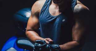 Athletic man in tank top beside a blue motorcycle in dim lighting.