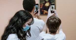 A group of people capturing a humorous, masked Mona Lisa painting with smartphones indoors.