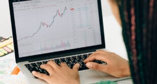 A woman working on financial analysis using a laptop with a stock market graph on screen.