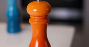 Bright orange and red pepper grinder on a modern kitchen table.