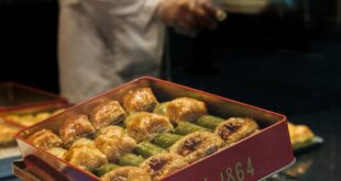 A display of assorted Turkish baklava in a bakery with a vendor in the background.