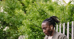 Young man focused on laptop work sitting on a park bench under a bridge.