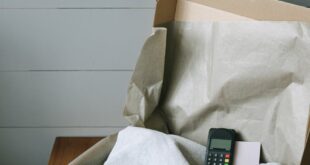 Cardboard box containing a folded shirt and a payment terminal, perfect for e-commerce themes.