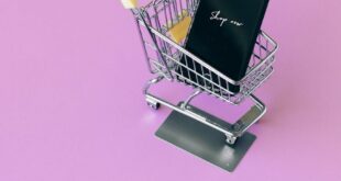 Mobile phone in mini cart on pink surface, symbolizing online shopping.