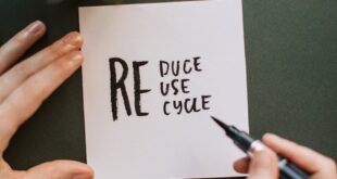 Close-up of hands writing a motivational 'Reduce Reuse Recycle' note on paper with a pen, surrounded by office items.
