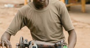 A skilled tailor sewing clothes on a traditional sewing machine on a Kumasi street.