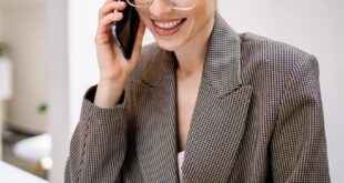 Confident businesswoman wearing glasses, talking on phone while reviewing documents in modern office setting.