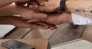 Hands from a diverse team stack on a table symbolizing unity and teamwork in a modern office setting.