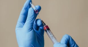 Close-up of gloved hands preparing a syringe with a vaccine indoors.