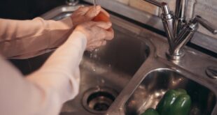 Person washing fresh vegetables under running tap water in a kitchen.