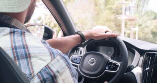 Man in casual attire driving a Volvo car, focused on steering wheel and dashboard.
