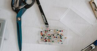 Top view of small plastic box with pins and scissors placed on table with sewing supplies in modern light workshop