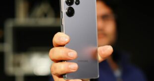 A person holding a Samsung smartphone with focus on the device, indoors.