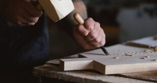 A craftsman skillfully using a mallet and chisel to carve wood in a workshop.