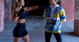 Two people engage in a playful fitness interaction under a brick archway.