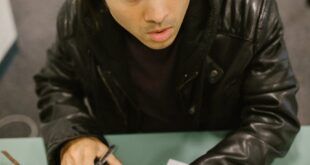 College student using a calculator and test paper, possibly during an exam or study session, in a classroom setting.