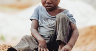 A young Ghanaian child sits playfully on a pile of rocks, embodying simplicity and joy.