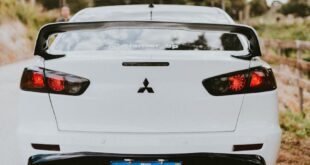 Dynamic rear view of a white sports car on a rural road, showcasing its sleek design.