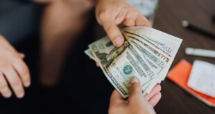 A close-up view of hands exchanging dollar bills indoors, symbolizing payment.
