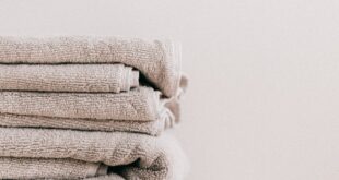 Stack of soft clean fresh gray towels placed on white minimalist stool against beige wall