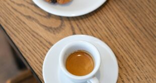 Flat lay of a fresh espresso and croissant on a wooden table.