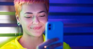 A stylish young woman with short hair using smartphone in vibrant neon lighting.