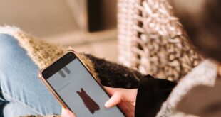 A woman comfortably browsing online shopping for a dress using her smartphone, enjoying leisure time indoors.