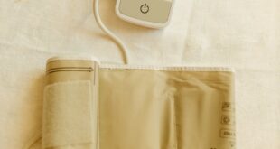 Top view of a digital blood pressure monitor and cuff on white fabric background.