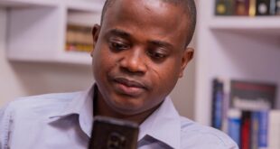 Focused African professional using smartphone in a modern office setting.