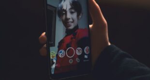 Close-up of a person taking a selfie at night using a smartphone, featuring the phone screen and their reflection.