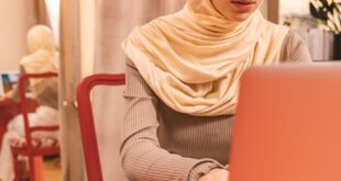 Focused Middle Eastern woman in hijab using a laptop at a vibrant indoor setting with reflective decor.