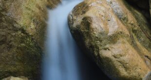Long exposure of a tranquil waterfall flowing over large rocks in a natural setting.
