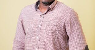 Fashionable portrait of a man in Accra, Ghana wearing a checkered shirt against a yellow background.